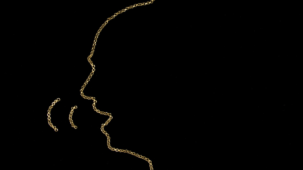 A still from Rafael Aflalo Rodes’ “Billy and Charley” — a silhouette of a face made from gold chains in a black background that appears to be speaking.