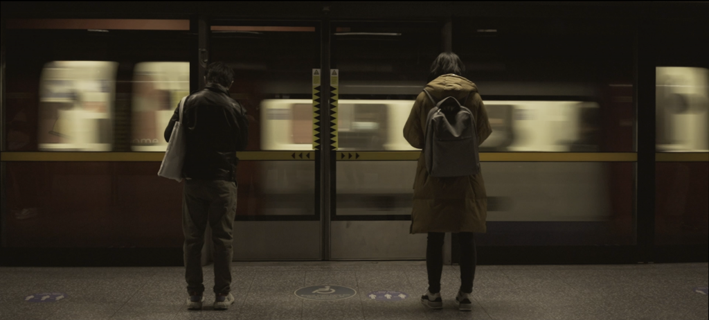A still from Soham Kundu’s “Stay Maybe? We Think We Made a Film” — two people waiting for a train in the underground, as another train passes